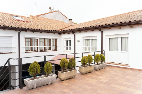A building with a tiled roof, white walls, and multiple windows. There are five rectangular planters with small trees on the ground floor. - Accommodation for groups and village with special charm, 20 minutes from LEÓN. (Cimanes del Tejar)