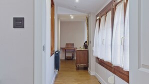 Un pasillo con suelo de madera, un radiador, una mesa con una cesta y un espejo con cortinas.