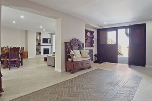 Un vaste espace de vie agrémenté d’un tapis à motifs en chevrons, d’un canapé en bois et d’un téléviseur fixé à un mur en pierre.