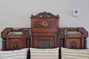 Un lit en bois avec une tête de lit sculptée, une table de chevet et un thermostat fixé au mur.
