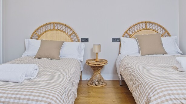 Una habitación con dos camas individuales, cada una con cabecera, mesita de noche y lámpara.