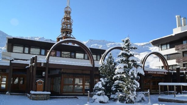A snow-covered building with a ski lift tower, wooden entrance, and a sign for the Office de Tourisme.