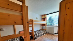 A dormitory room with bunk beds, a window with curtains, and a radiator.