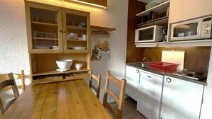 Una cuina compacta amb una taula de fusta, armaris blancs, un microones i un rentaplat.