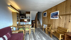 Un espai habitable compacte amb cuina americana, mobiliari de fusta i una escala que condueix a un altre nivell.