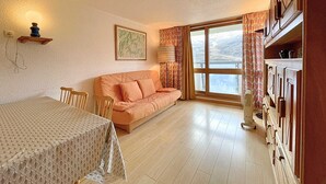 A cozy room with a sofa, a dining table, and a large window with curtains.
