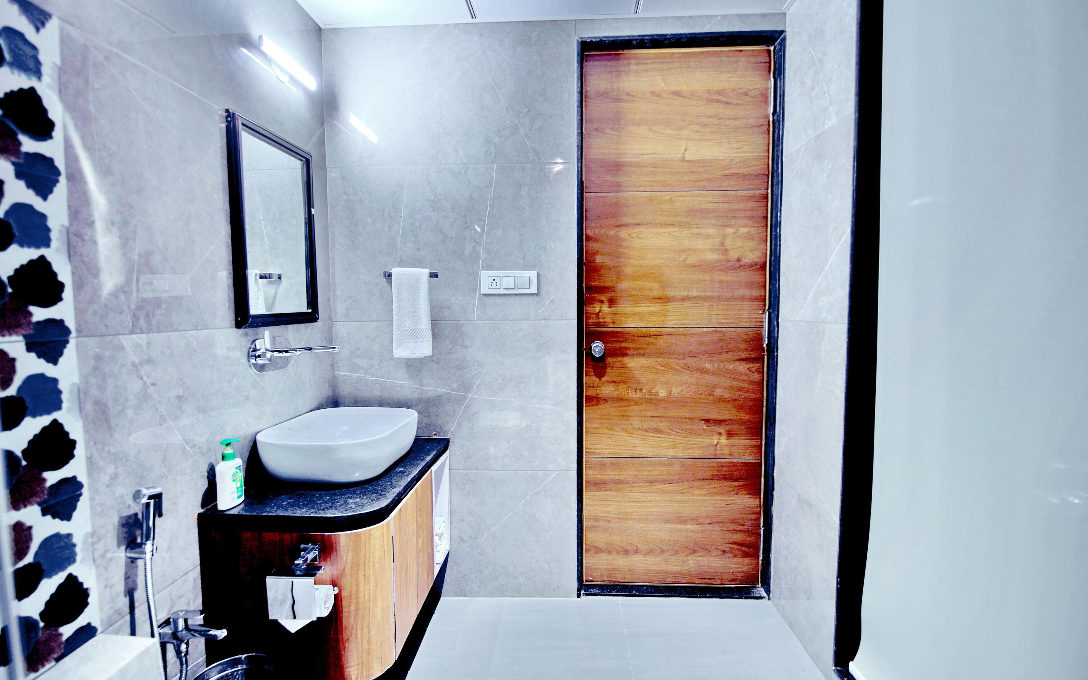 A modern bathroom with a wooden door, a sink with a mirror above it, and a towel rack.