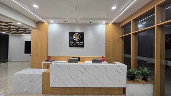 A reception desk with a logo for 'Anil Farm's Gir Jungle Resort', two chairs, a potted plant, and a wooden panel wall.