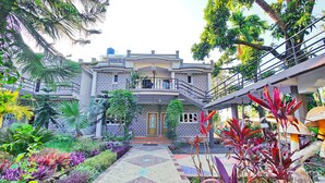 Um edifício de dois andares com um pátio central, rodeado por vegetação exuberante e um caminho decorativo.