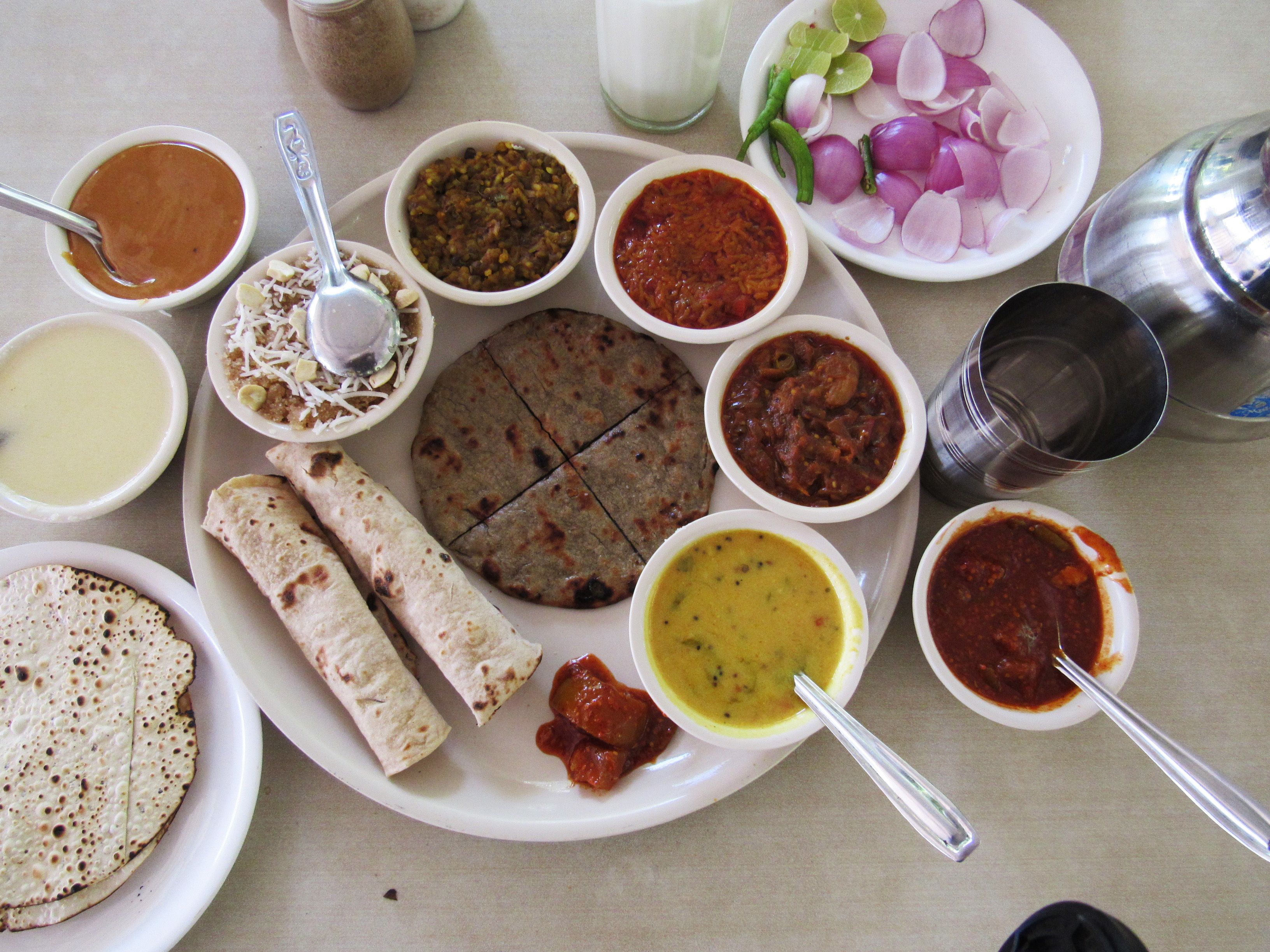 A variety of dishes and condiments on a table, including flatbreads, soups, and a plate with sliced onions and lime.