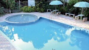 Uma piscina com borda de pedra, rodeada por um terraço de tijolos e guarda-sóis verdes.