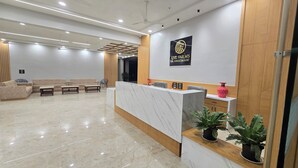 Uma área de recepção de hotel com balcão de mármore, um logotipo na parede e um espaço de estar com sofás e cadeiras.