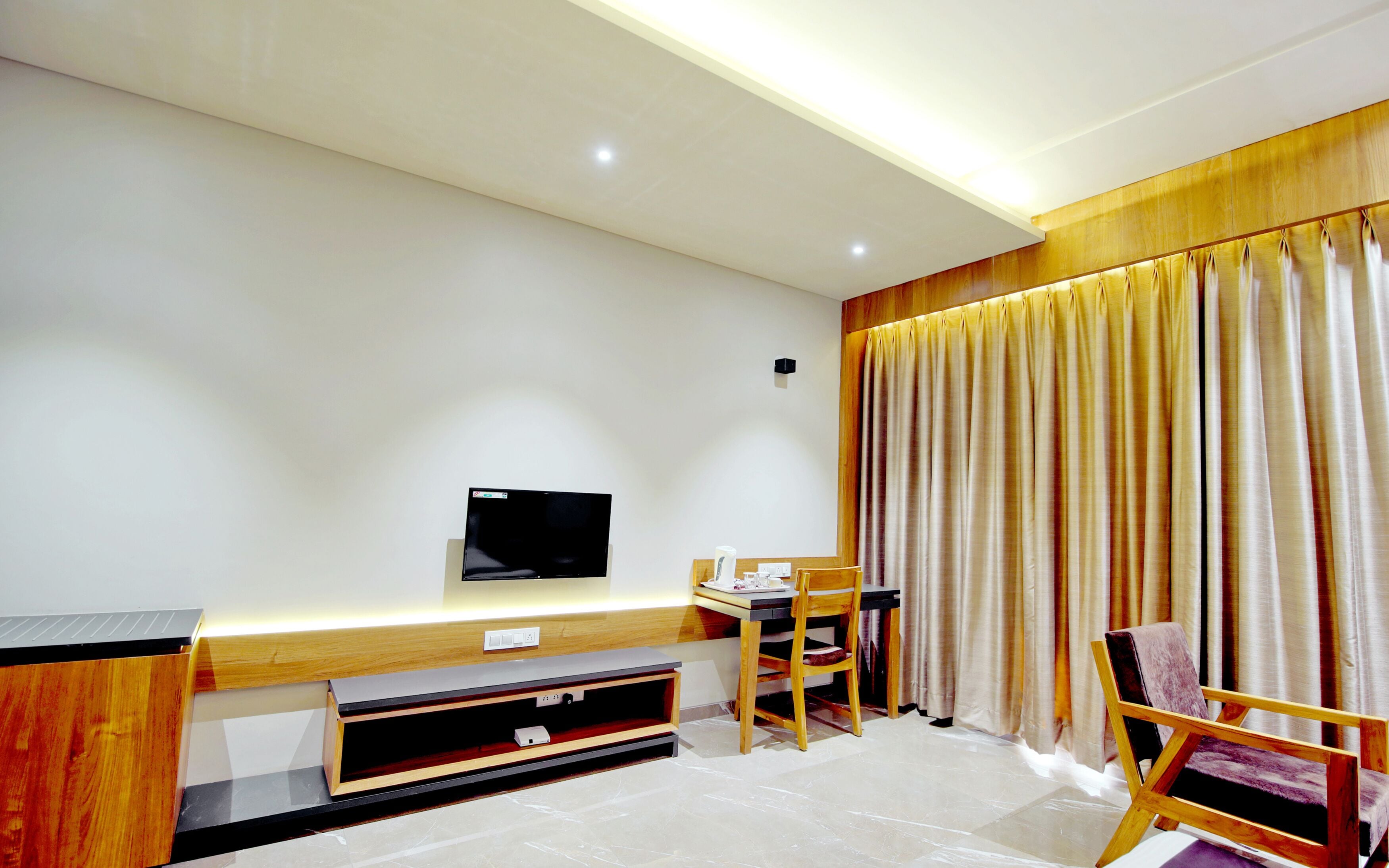 Una sala moderna con un televisor de pantalla plana montado en la pared, un mueble de madera para entretenimiento, una mesa de comedor con sillas y un ventanal con cortinas.