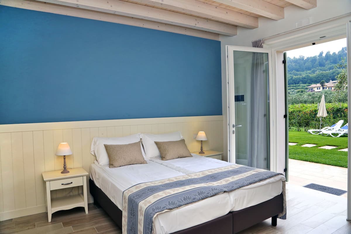 A bedroom with a bed, bedside tables, and a view of the garden.