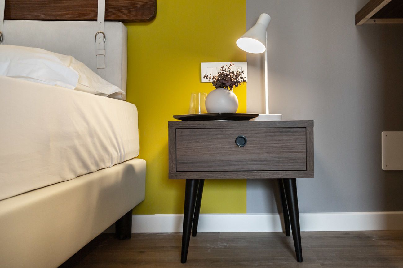 A bedroom with a bed, a nightstand with a lamp, and a vase with flowers.
