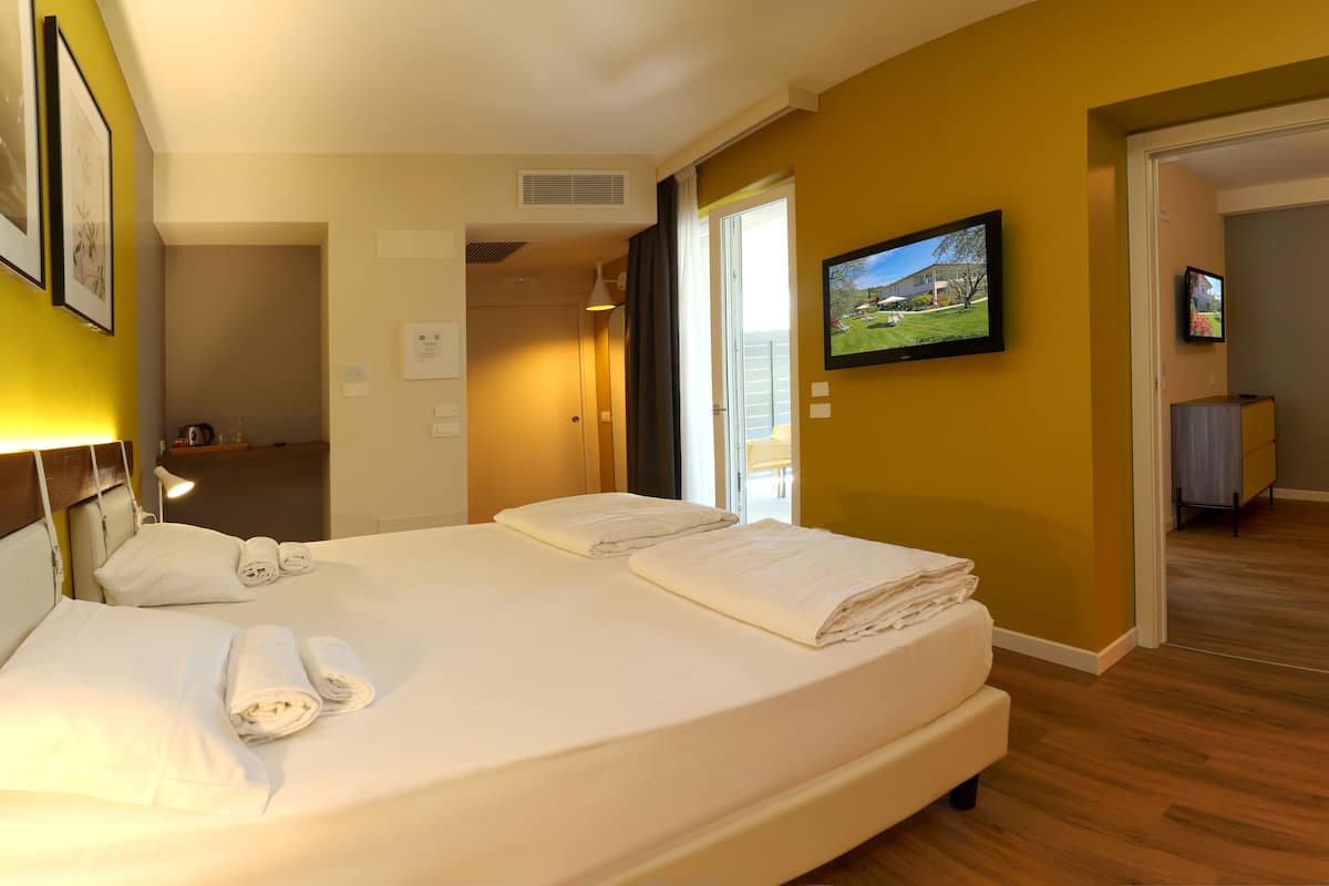 A hotel room with a bed, a TV, and a view of the outside.