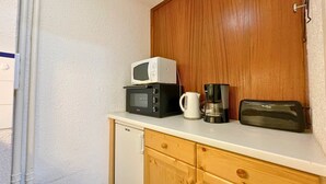 Pieni, käytännöllinen keittokomero, jossa on mikroaaltouuni, kahvinkeitin ja leivänpaahdin, ja kaikki sijoitettu valkoiselle työtasolle.