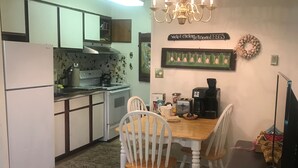A compact kitchen with white cabinets, a dining table with chairs, a chandelier, and a coffee maker.