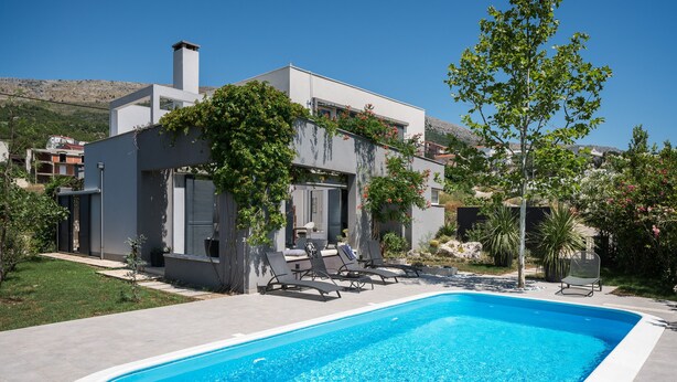 Une maison moderne dotée d’une piscine, d’un espace de détente extérieur et d’un jardin.