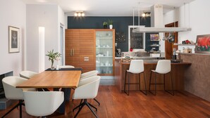 Une cuisine moderne avec des meubles en bois, un coin repas avec une table en bois et des chaises blanches, et un petit coin bar.