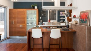 Une cuisine moderne avec des meubles en bois, un îlot central doté de tabourets, une grande fenêtre et un porte-casseroles suspendu.