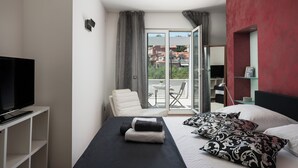 Une chambre d’hôtel moderne équipée d’un lit, d’une télévision, d’une chaise et d’un balcon offrant une vue sur les bâtiments.