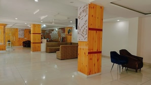 Un hall d’entrée spacieux avec un plafond haut, des piliers en bois, un comptoir d’accueil et un espace détente avec des canapés et des fauteuils.