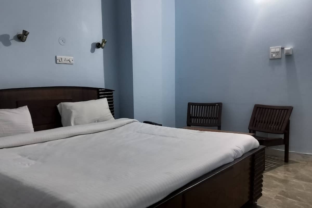A neatly made bed with white linens in a room with light blue walls, a wooden headboard, and two wooden chairs.