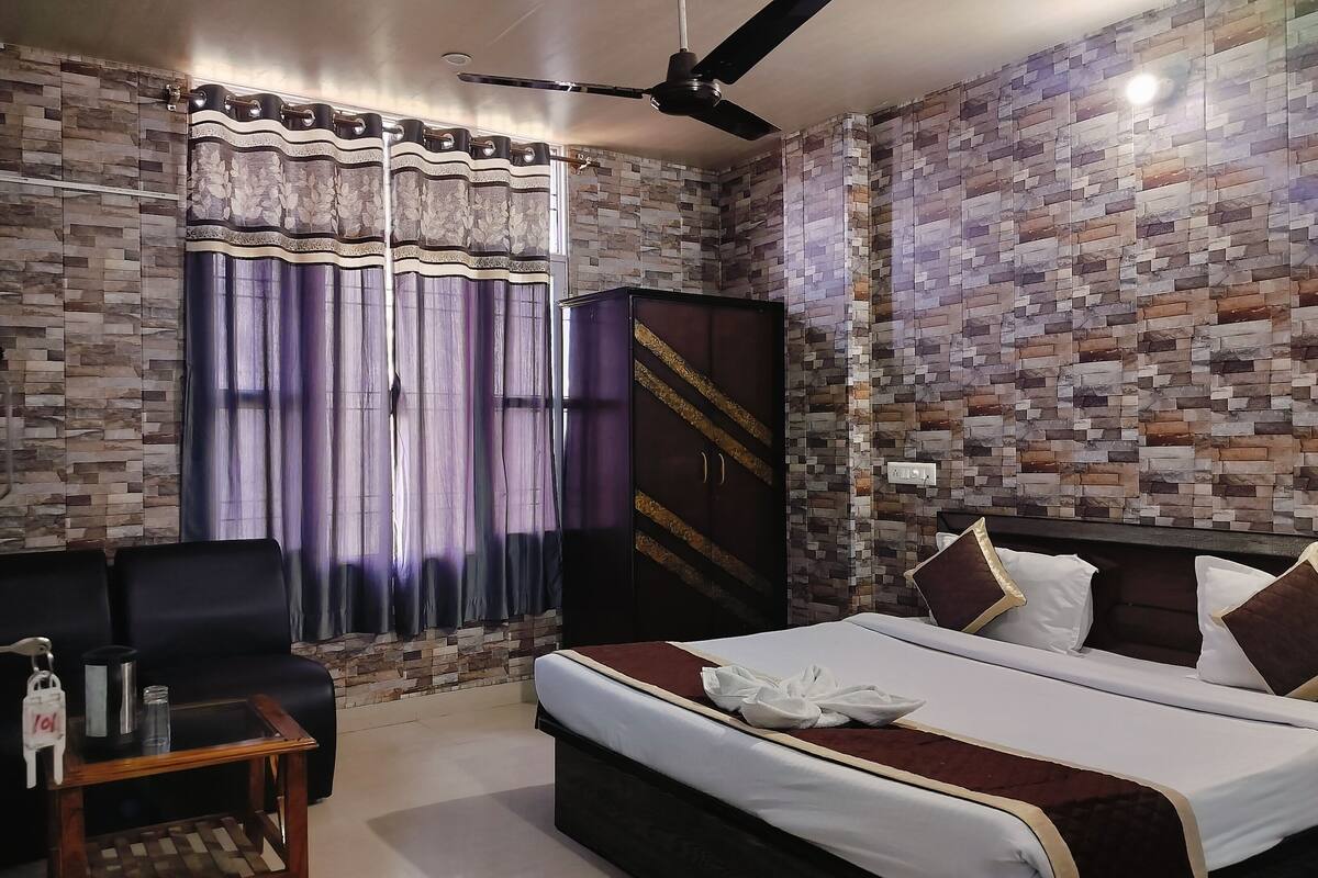 A hotel room with a bed, a desk, a chair, a wardrobe, and a ceiling fan.