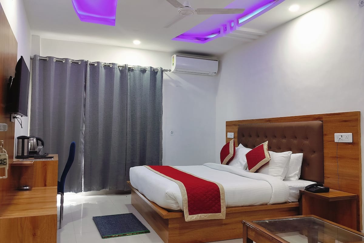 A hotel room with a bed, bedside table, TV, air conditioning unit, and a ceiling fan.
