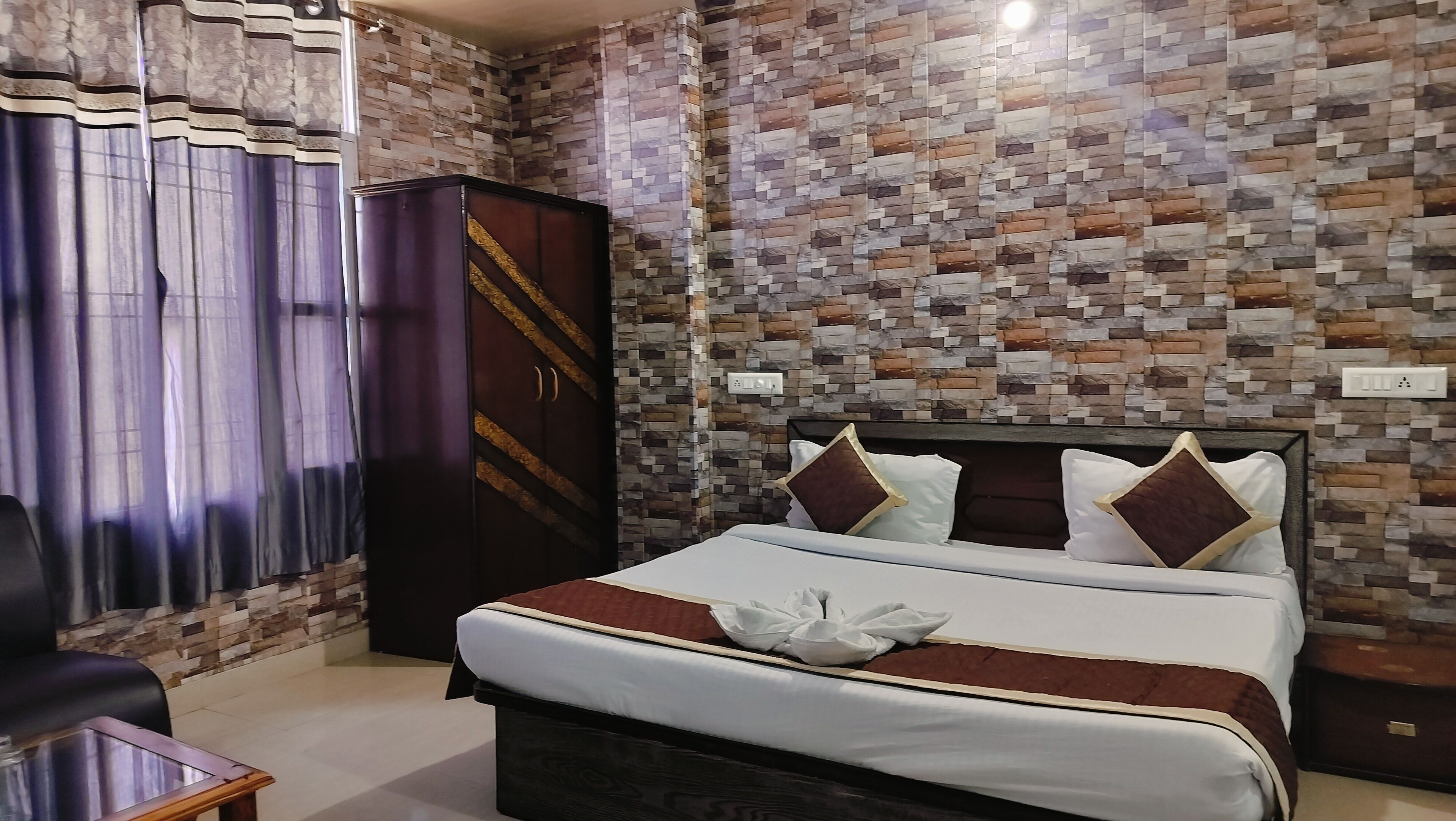 A hotel room with a bed, curtains, a wardrobe, and a wall with a mosaic pattern.
