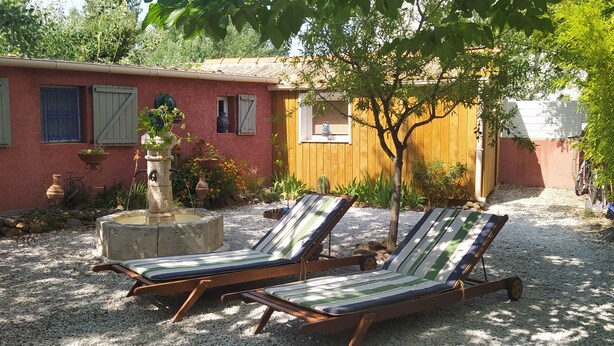 A patio with two striped lounge chairs, a small fountain, and a red building with blue shutters.