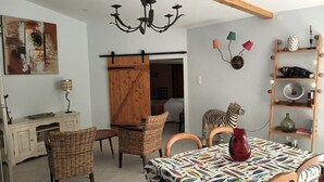 A cozy room with a dining table, wicker chairs, a zebra statue, a chandelier, and a wooden shelf with decorative items.