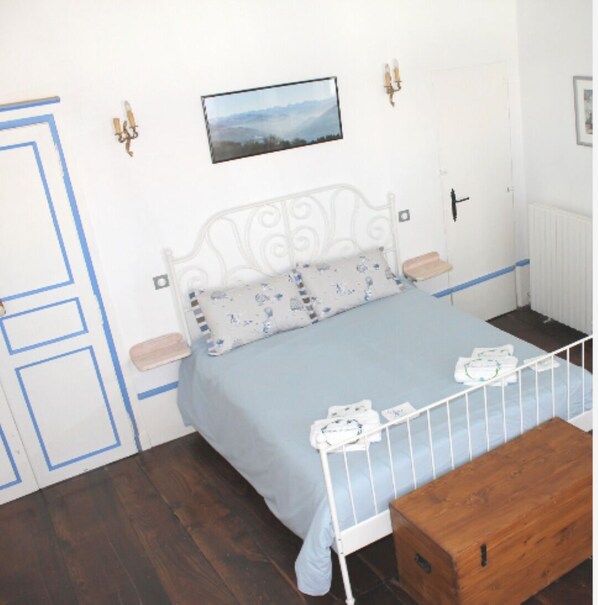 A bedroom with a bed, a wooden bench, a white radiator, and a framed picture on the wall. - VINCENT REGAGNON room (Saint-Girons)