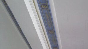 Un coin de pièce aux murs blancs, avec une bordure décorative bleue au plafond.