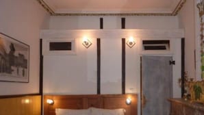 Une chambre d’hôtel avec un lit, une tête de lit en bois, une porte et un luminaire fixé au mur.