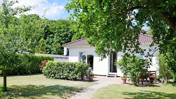 A white building with a tiled roof, a paved pathway leading to the entrance, and a bench in the foreground. - Holiday Falkenhagen with garden (Sundhagen)