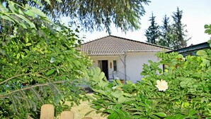 A house with a tiled roof, surrounded by lush greenery and a wooden fence. - Holiday Falkenhagen with garden (Sundhagen)
