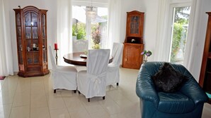 A dining area with a round table, white chairs, a blue leather sofa, and two wooden cabinets. - Holiday Falkenhagen with garden (Sundhagen)