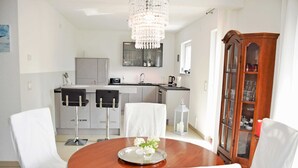 A modern kitchen with a dining area, featuring a chandelier, white chairs, and a wooden dining table with a floral centerpiece. - Holiday Falkenhagen with garden (Sundhagen)