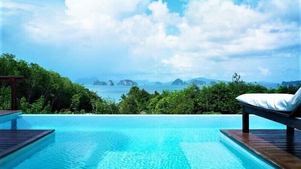 Una piscina infinita con terraza de madera, una silla de descanso y vista al océano y a las islas.
