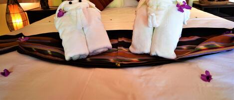 Una cama con dos toallas con forma de osos, una mesita de noche con lámpara y un cuenco decorativo en la mesilla.