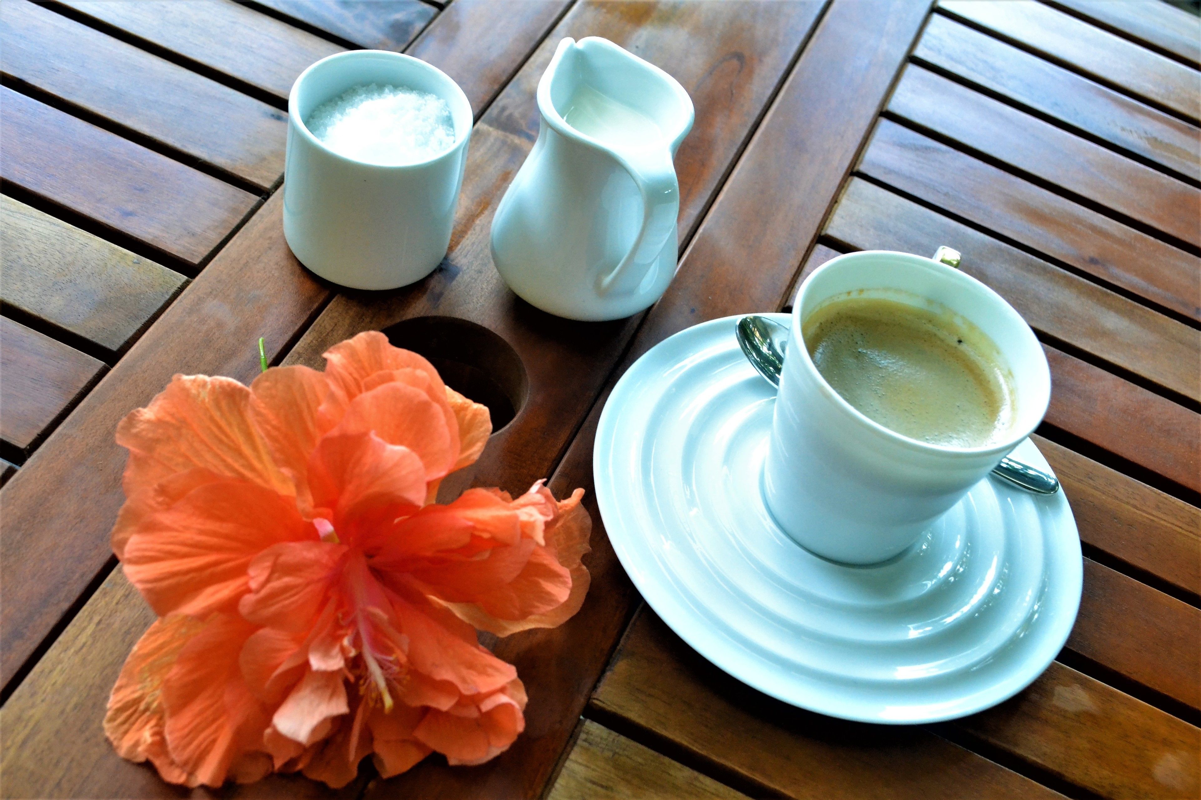 Ein Holztisch mit einer weißen Kaffeetasse, einer weißen Milchkanne und einer weißen Teetasse.