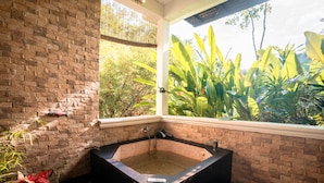 Un área de spa con una bañera grande, una ventana con vistas a la vegetación y una pared de ladrillo.
