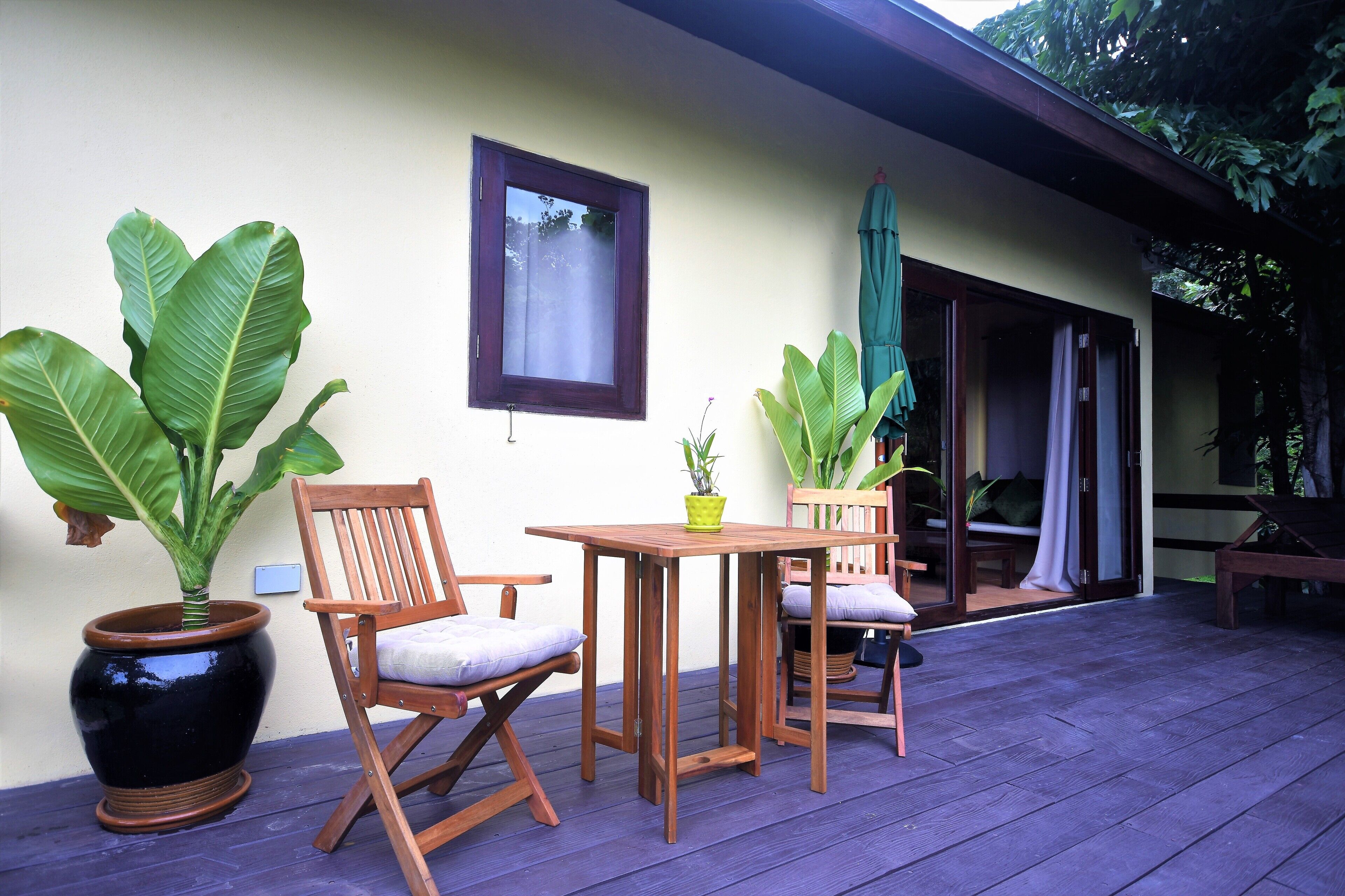 A wooden deck with a table and chairs, surrounded by large potted plants.