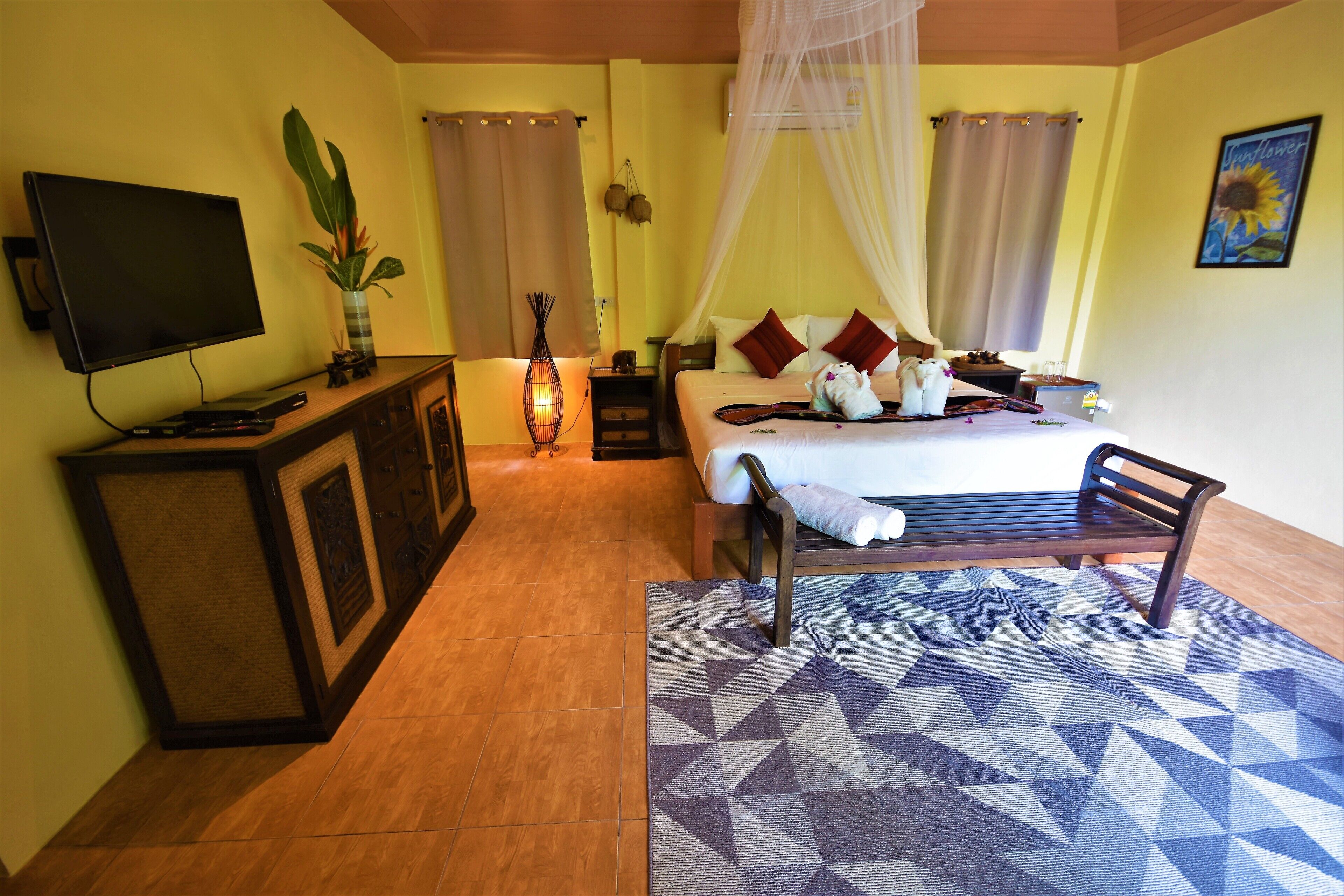 A bedroom with a bed, bedside table, TV, and a decorative plant.