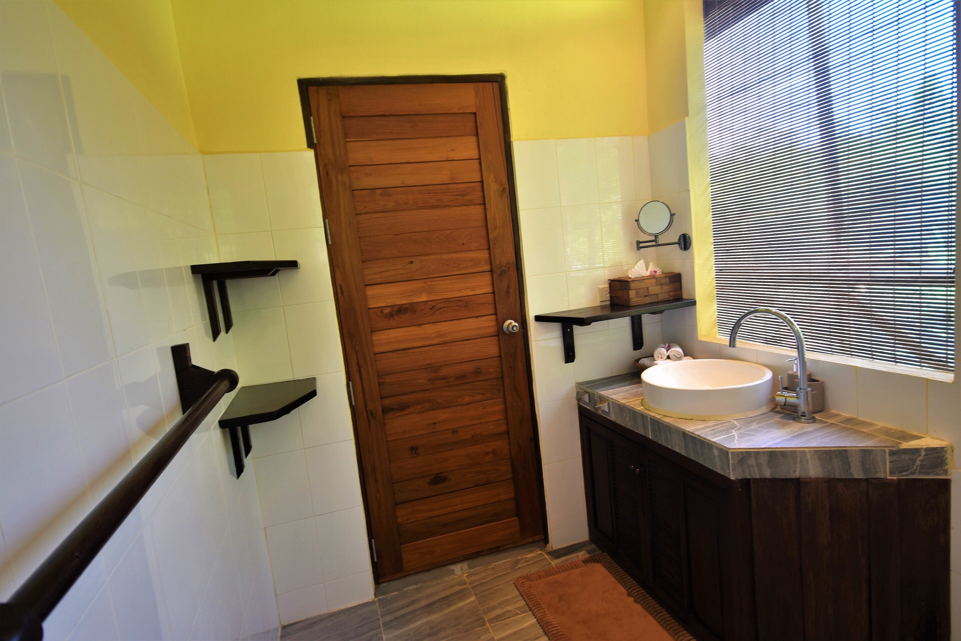 A bathroom with a wooden door, a sink with a mirror, and a window with blinds.