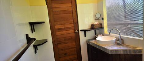 A bathroom with a wooden door, a sink with a mirror, and a window with blinds.