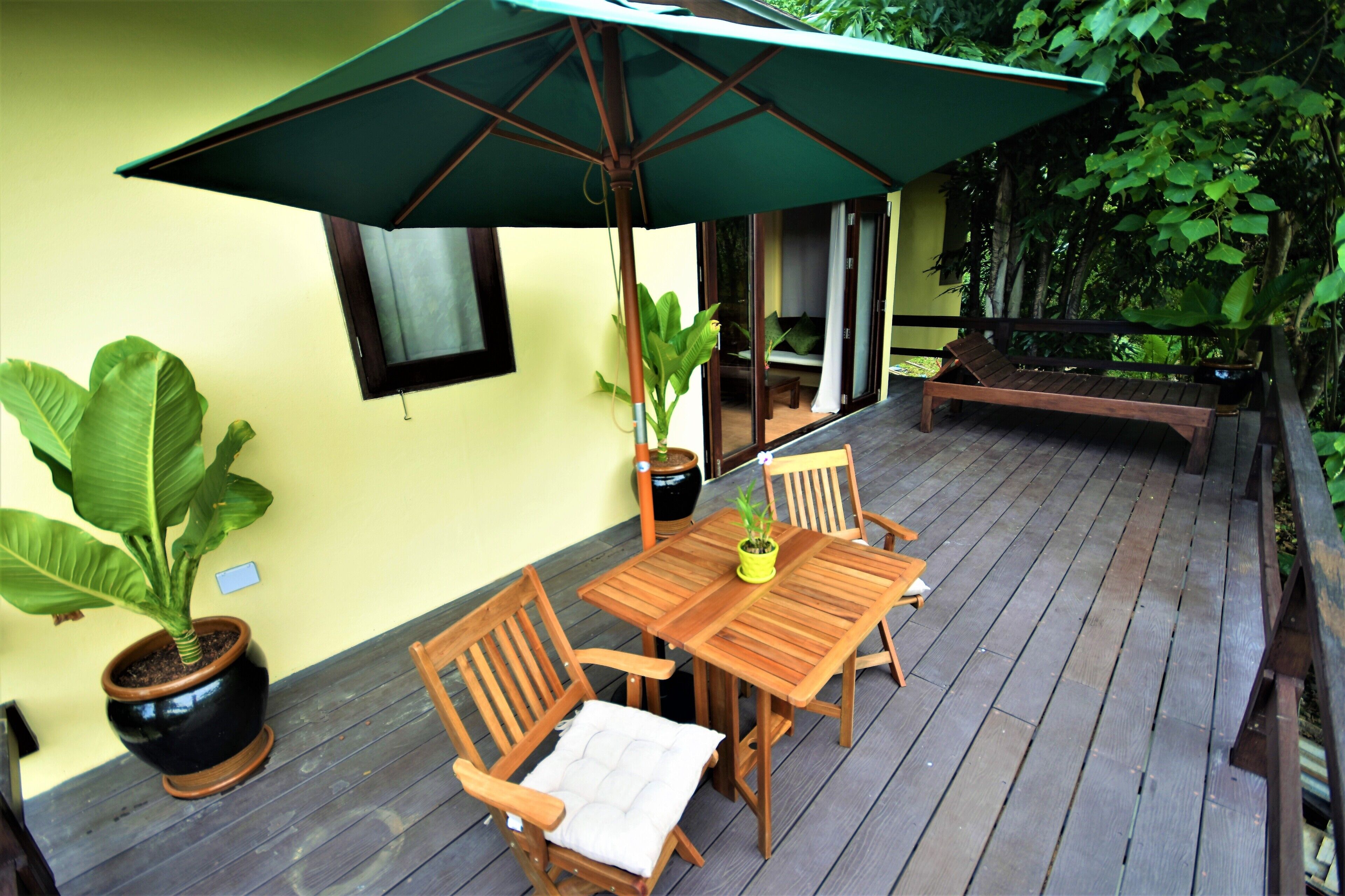 Una terraza de madera con una mesa, sillas, un paraguas verde y plantas en macetas.