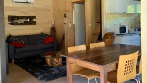 A wooden interior with a dining area, a sofa, and a kitchen visible through an open doorway. - Chalet du Moulin des Fontaines (Saint-Paul-les-Fonts)